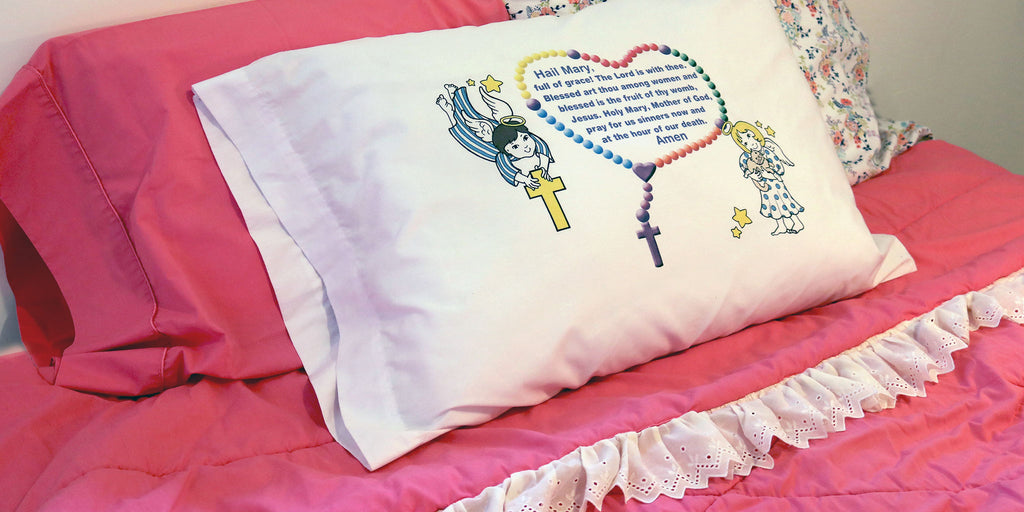 White pillowcase with cute angels and the Hail Mary Prayer is shown on a child's bed.