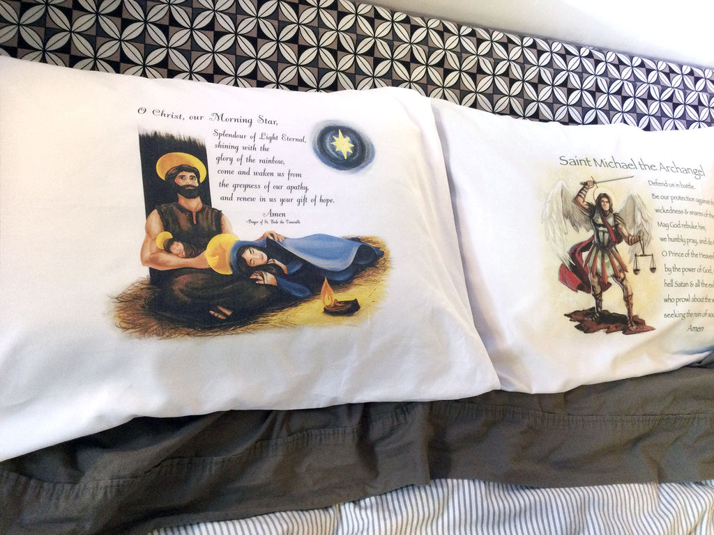 Two white pillowcases adorned with Catholic images of Holy Family and St. Michael with prayers