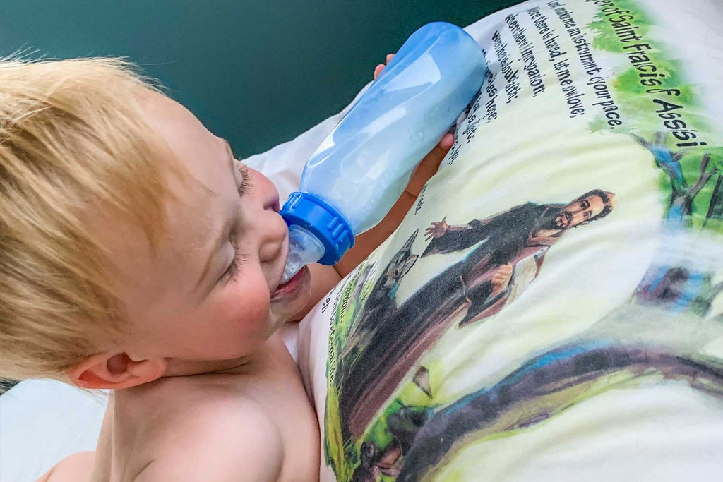 Happy toddler is enjoying his bottle with St. Francis pillow